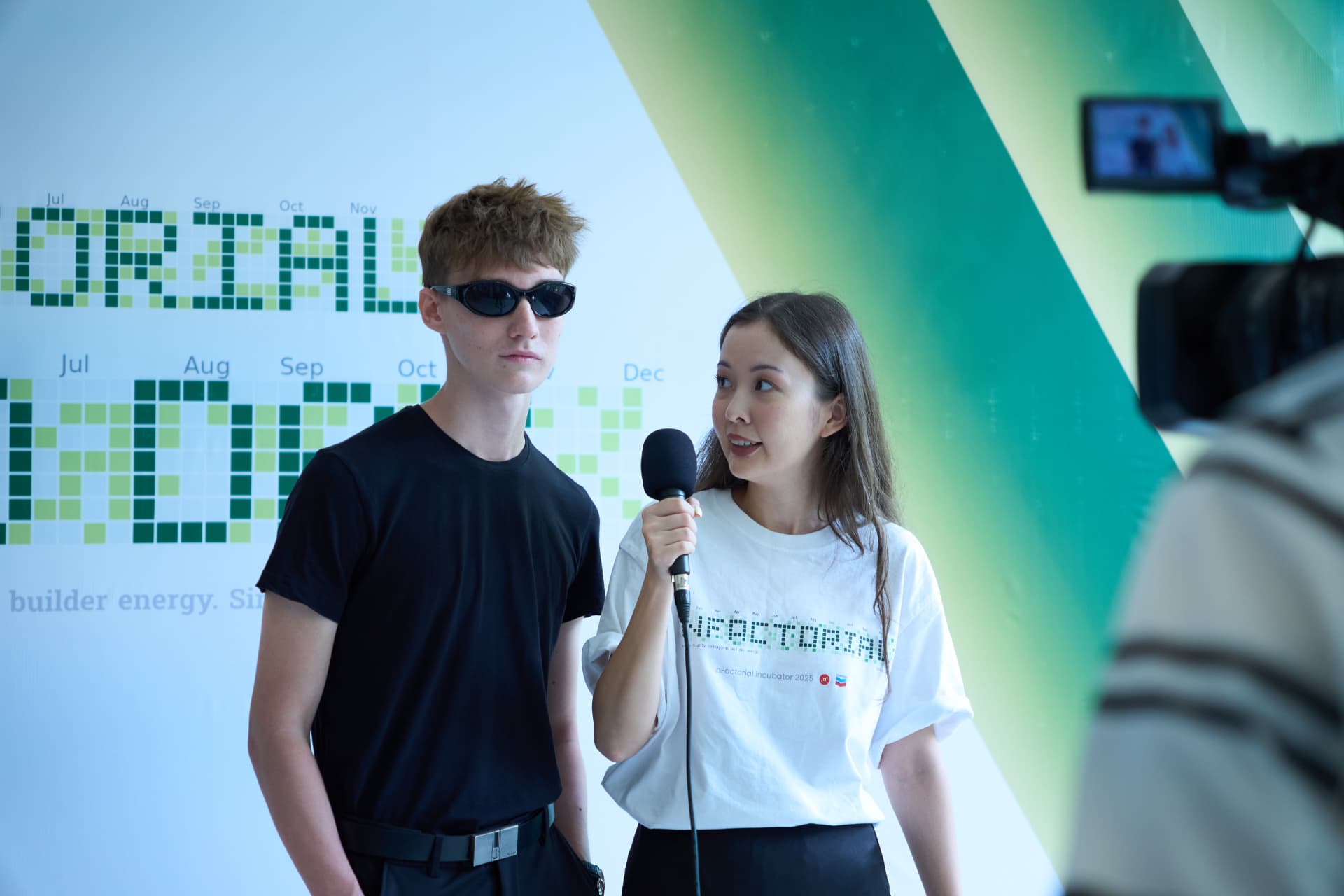 Участник nFactorial даёт интервью на фоне пресс-волла с графиком активности